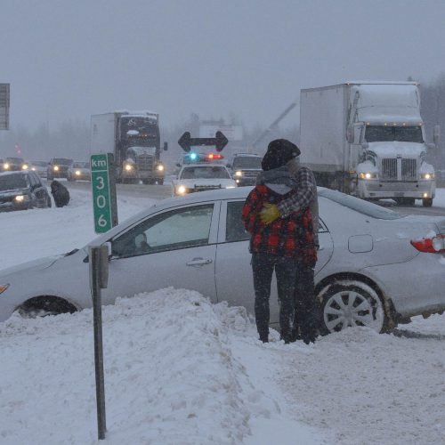 un couple enlacé devant leur auto dans la neige