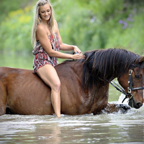 une femme blonde traverse l'eau à dos de cheval