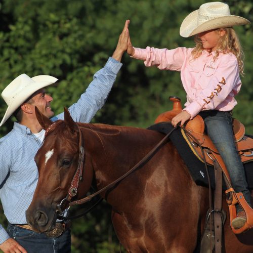 Un homme fait un high five à sa fille sur le dos d'un cheval brun