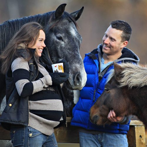 une femme enceinte avec une café à côté d'un cheval et un pony