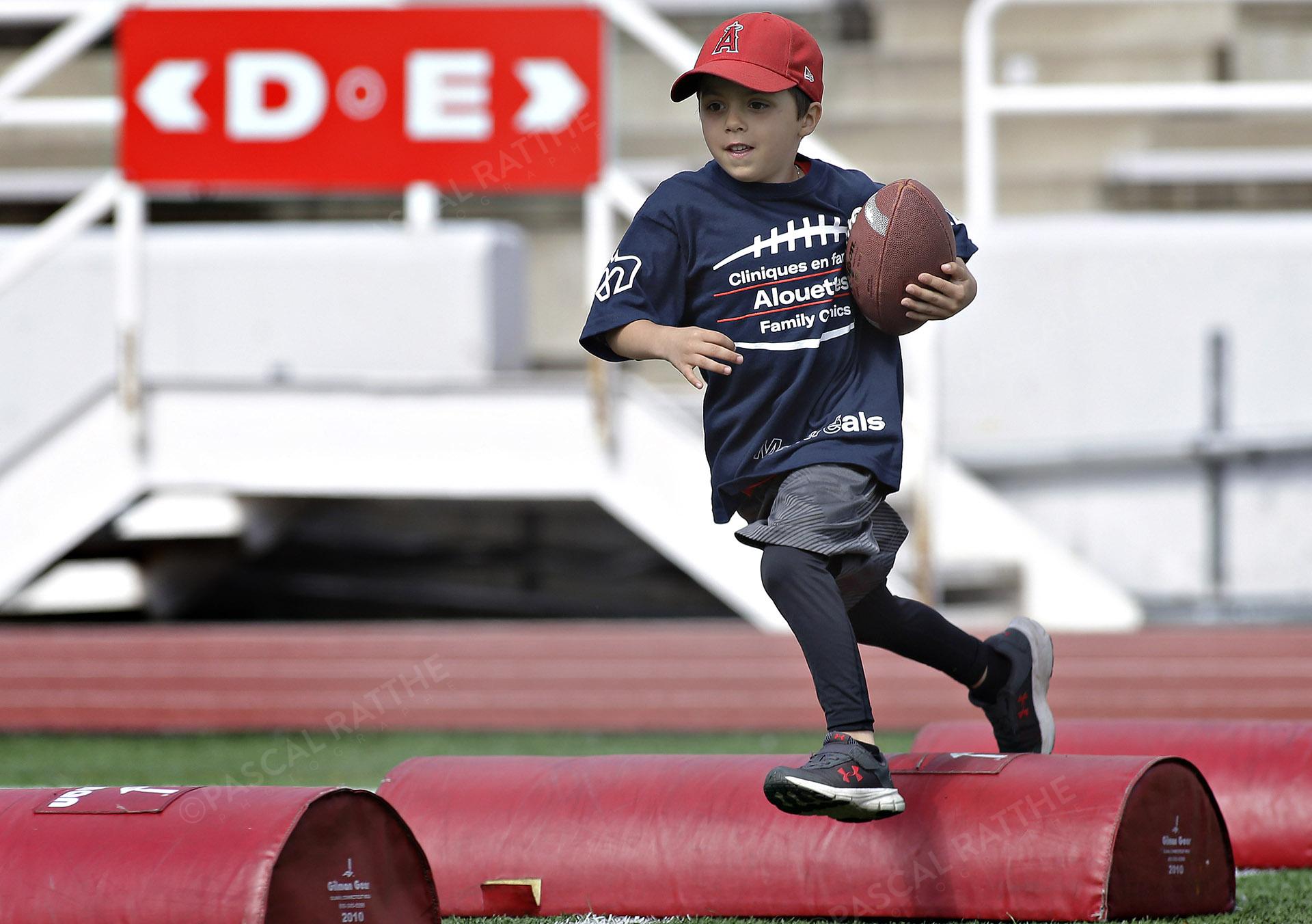 Cliniques Football des Alouettes de Montréal un jeune enfant saute avec un ballon par dessus un sac rouge