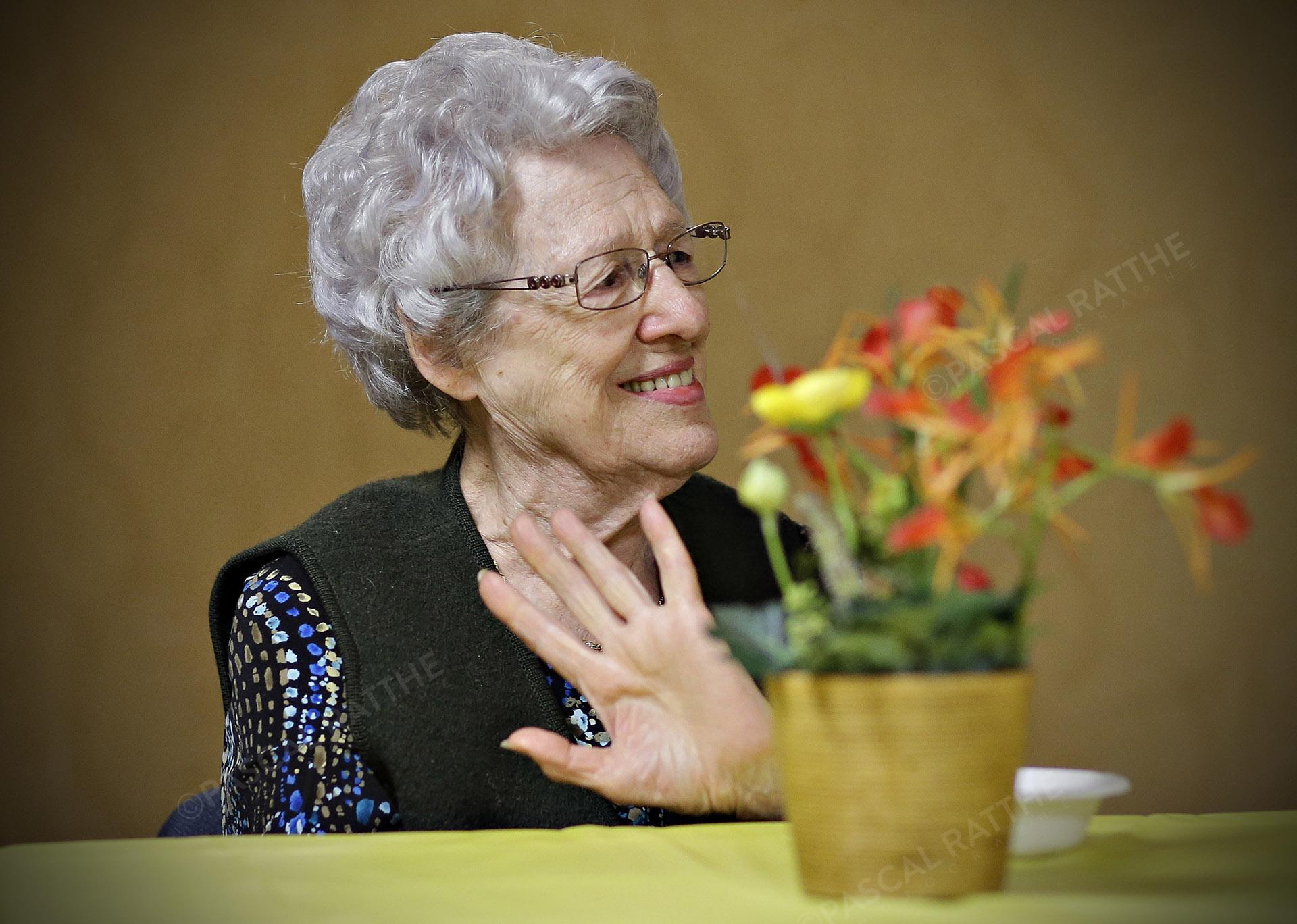 une dame du 3e âge avec un sourire éclantant et un pot de fleur sur la tête